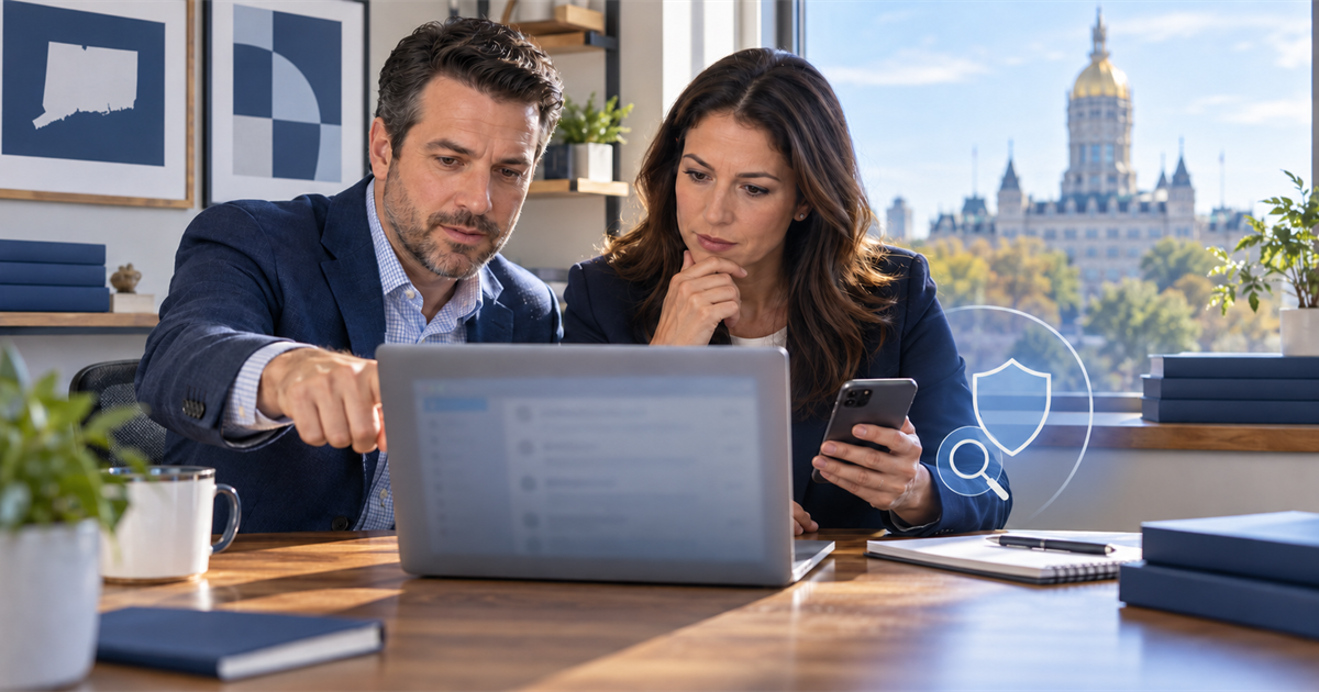 Two Connecticut business colleagues inspect an unreadable email on a laptop while verifying the request by phone.